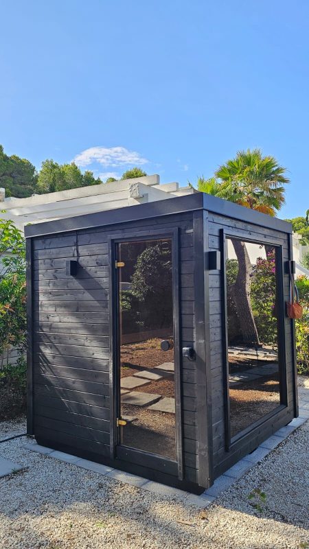 Lite Cube sauna in a Mediterranean garden, black timber cladding with glass door and side window